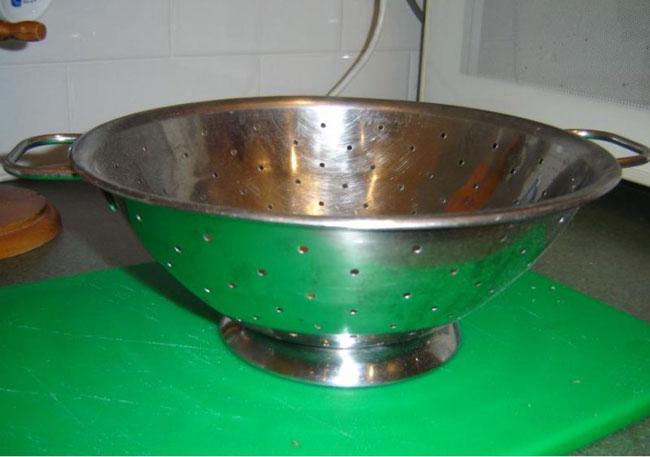 A sturdy stainless steel colander with perforated holes and ergonomic handles for draining